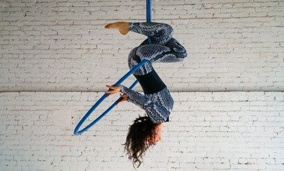 A young brunette woman is engaged in aerial acrobatics in a tracksuit on a white brick background. Sports concept. Balance.